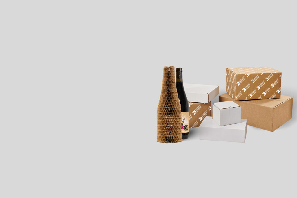 Eco-friendly packaging materials including cardboard shipping boxes, protective honeycomb paper wrap, and wine bottle mailers displayed on a neutral background