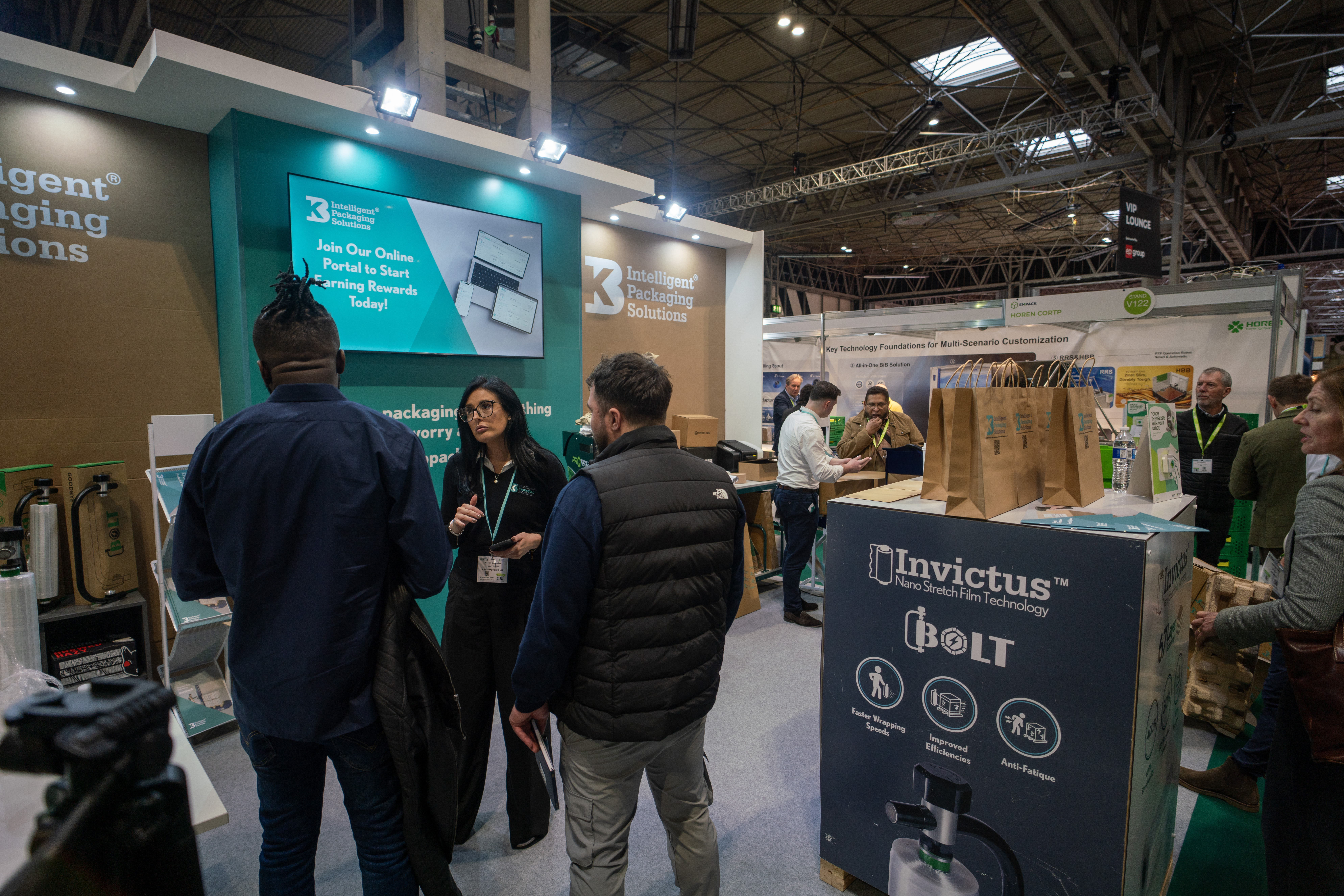 Busy exhibition stand at Packaging Innovations showcasing pallet wrapping and packaging solutions with visitors engaging in product demonstrations.