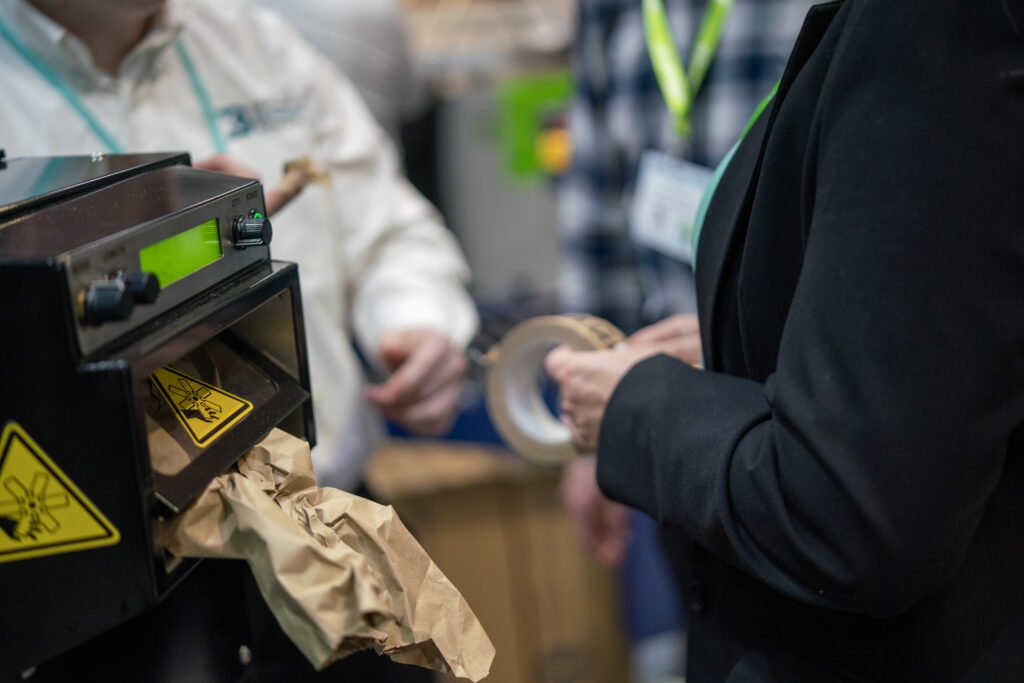 Operator using packaging tape and paper void fill at a packing station during a packaging process review.
