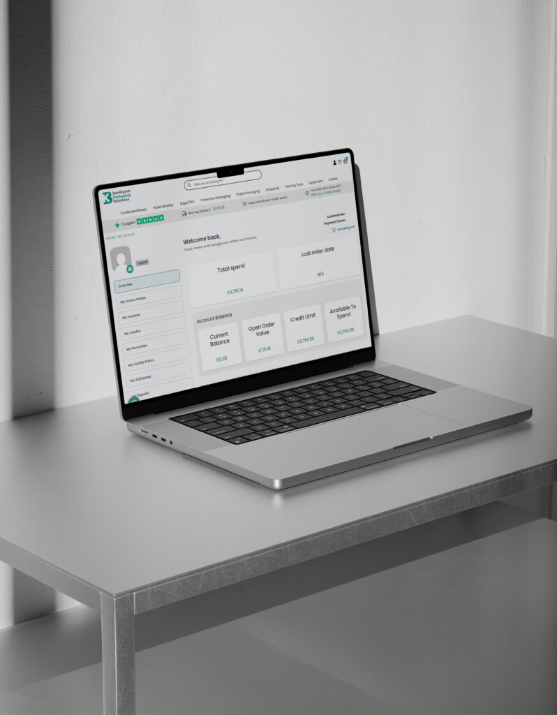 Laptop displaying the KB Packaging Online Portal dashboard, showing account information, order management tools, live pricing, and purchasing features on a desk in a modern office setting.