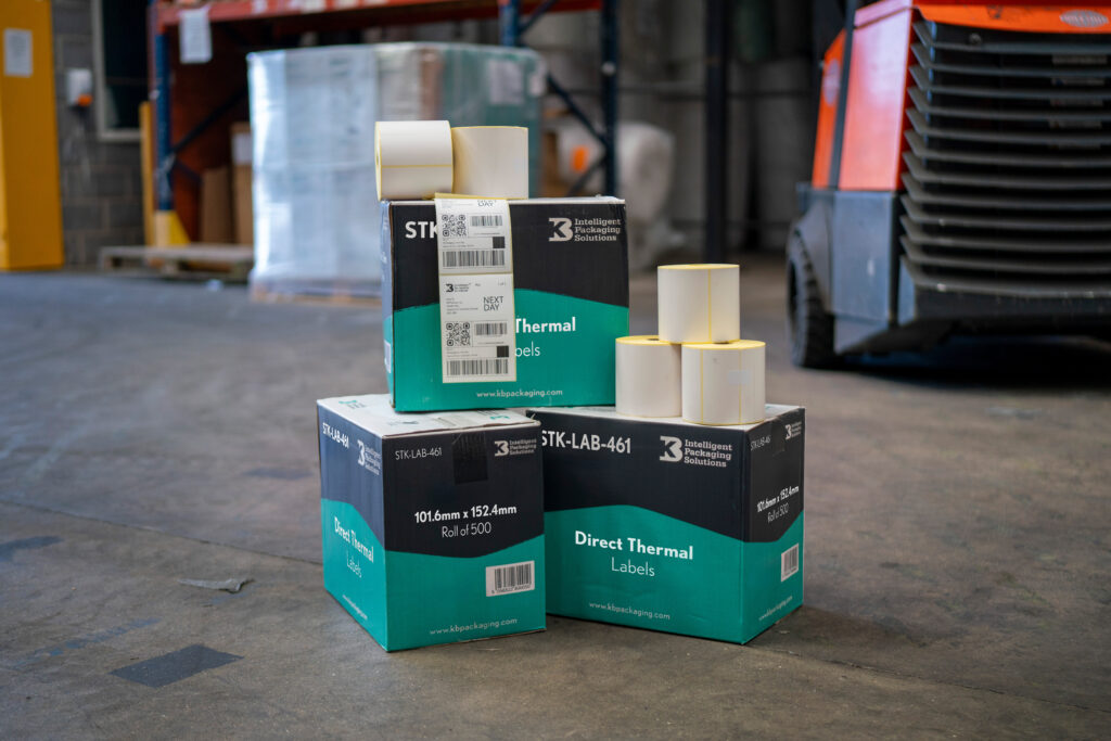 Boxes of direct thermal labels and label rolls displayed on a warehouse floor, with printed shipping labels applied to packaging.