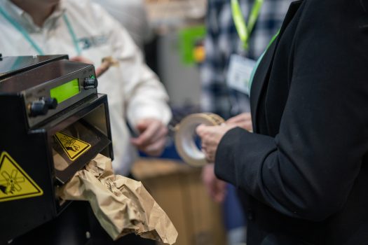 Operator using packaging tape and paper void fill at a packing station during a packaging process review.